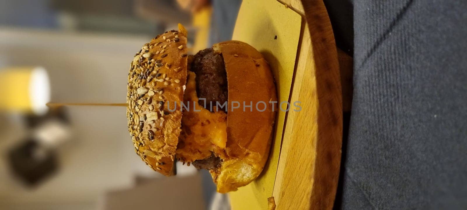Side view of a delicious cheeseburger with sesame bun, on a rustic wooden serving board