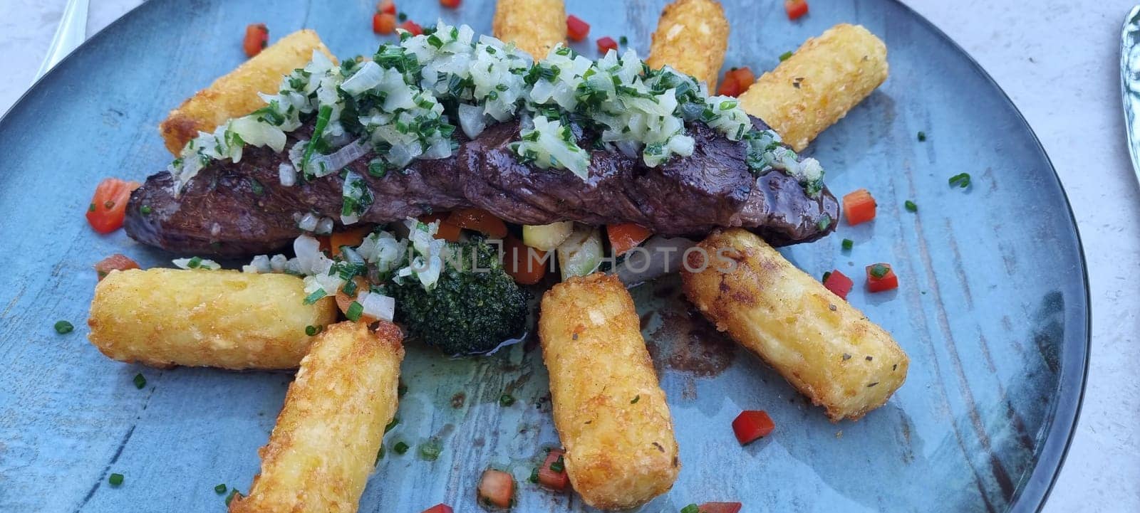 Grilled steak with herb topping served with golden polenta and fresh vegetables on a ceramic plate