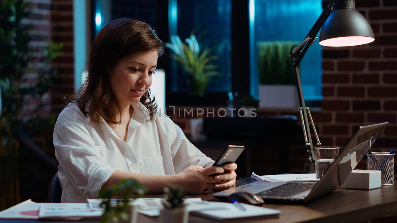 Smiling manager looking at text messages on smartphone, taking break from working on company project. Team leader unwinding by using phone to browse social media in office, camera B