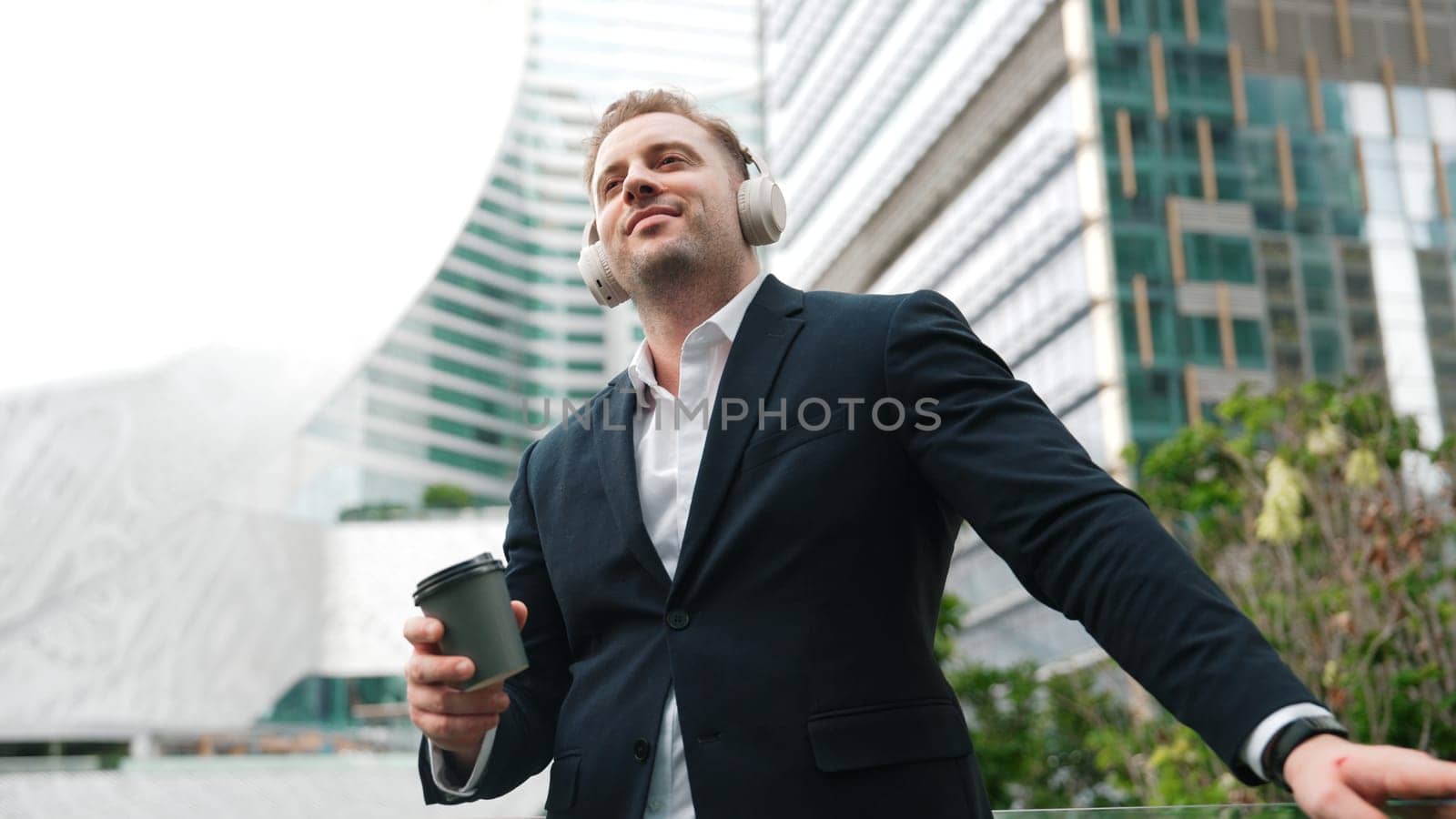 Close up of male leader listen headphone and dancing to relaxing music with cheerful and motivation. Skilled project manager enjoy to listen relaxed song while hold smart phone at urban city. Urbane.
