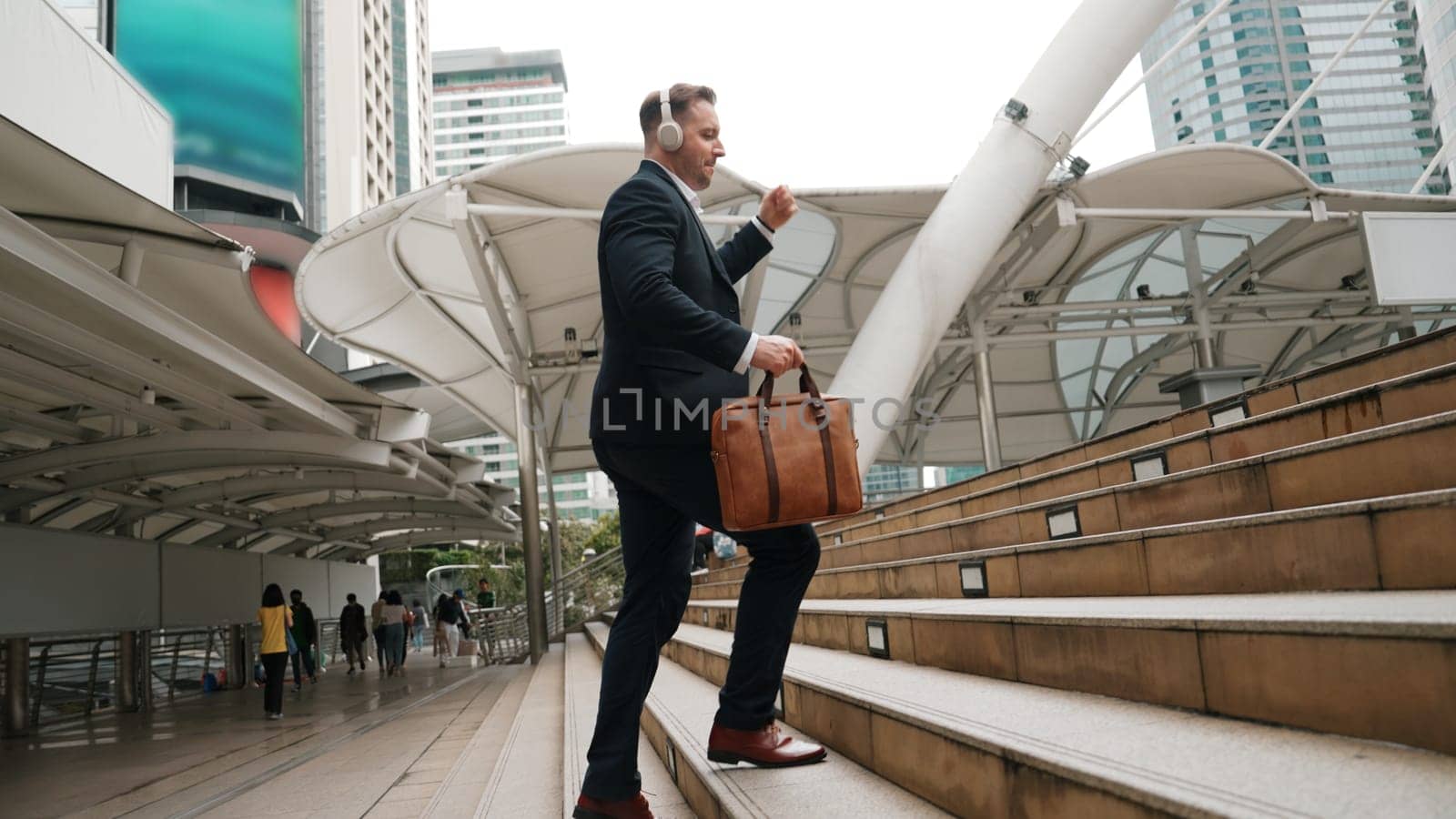 Smart caucasian businessman walking up stairs surrounded by urban view. Urbane. by biancoblue