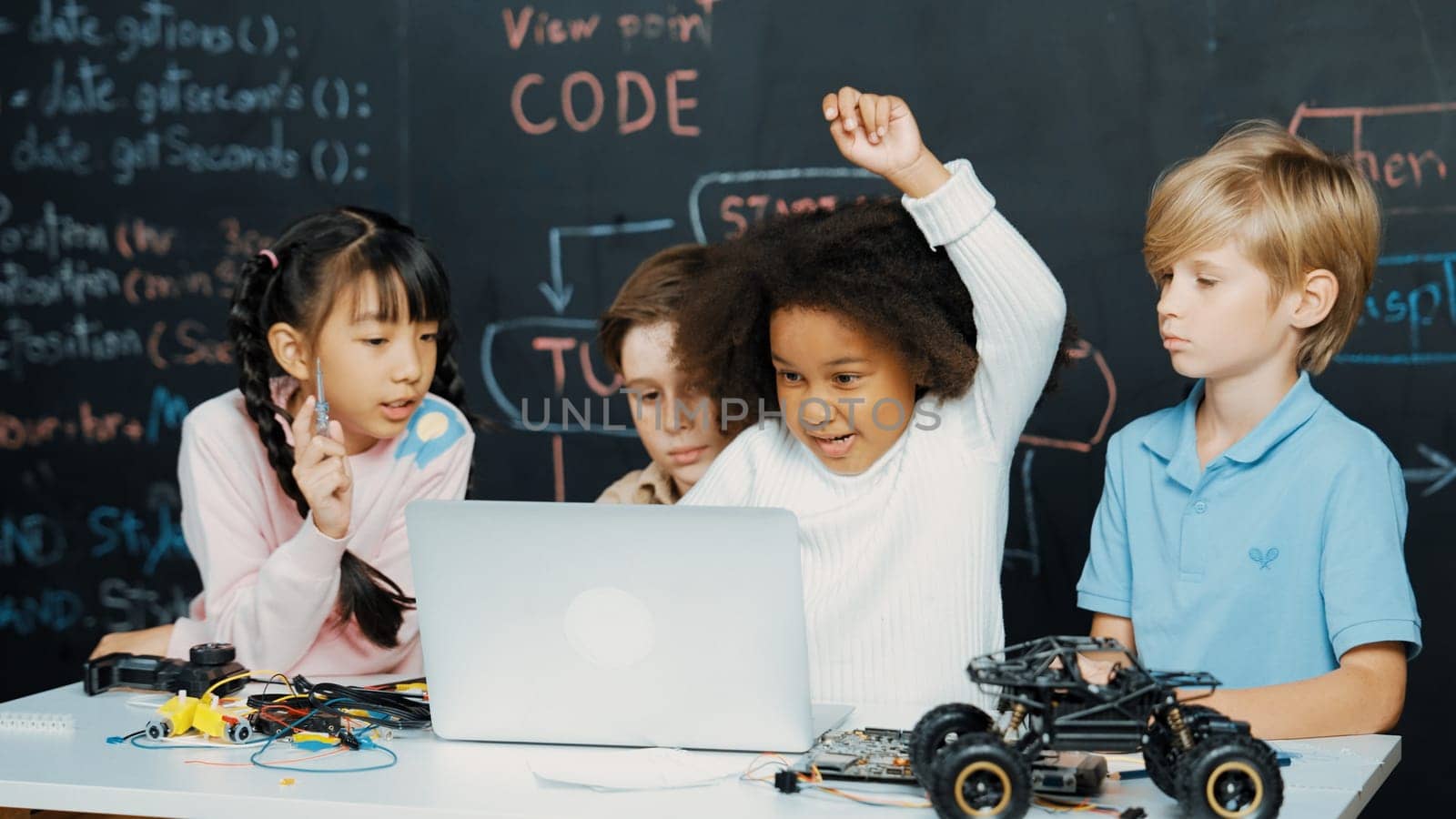 Multicultural smart children using laptop programing engineering code and writing or coding program in STEM technology classroom at blackboard written prompt. African girl raised hand. Erudition.
