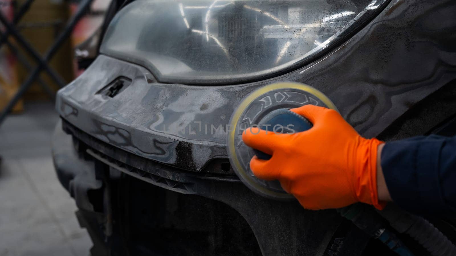 A mechanic sands the putty on a car body with a machine. Repair after an accident