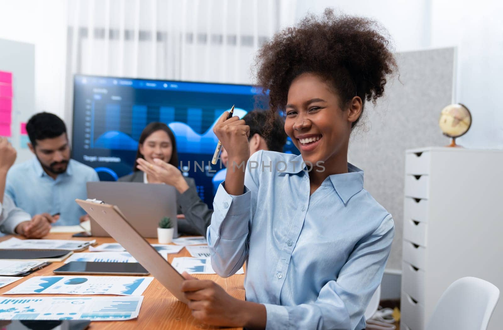 Portrait of happy young african businesswoman with group of office worker on meeting with screen display business dashboard in background. Confident office lady at team meeting. Concord