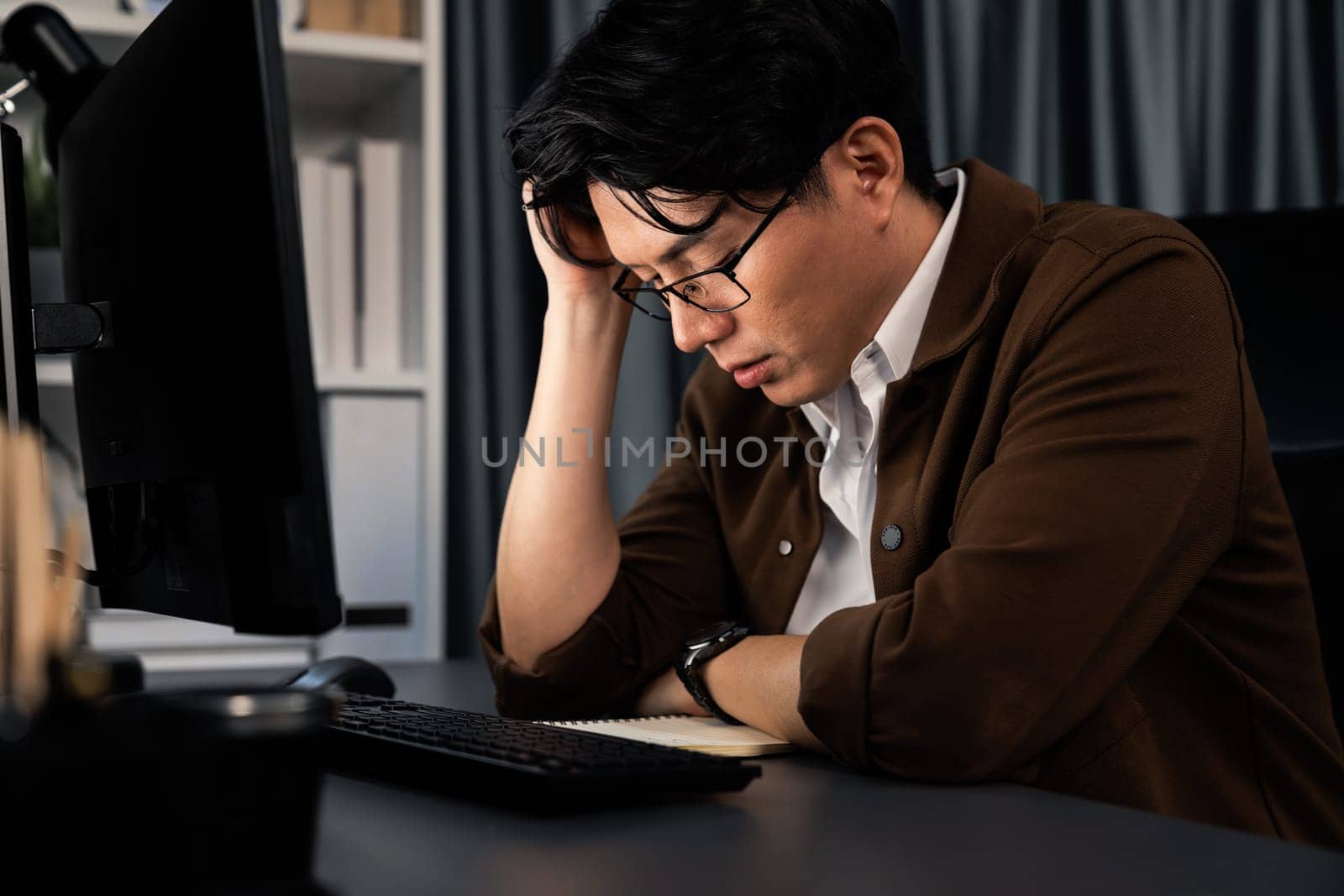 Smart businessman with stressful face working on pc waiting email from customer with making upper sales target revenue over late night time at office, working on startup company project job. Infobahn.