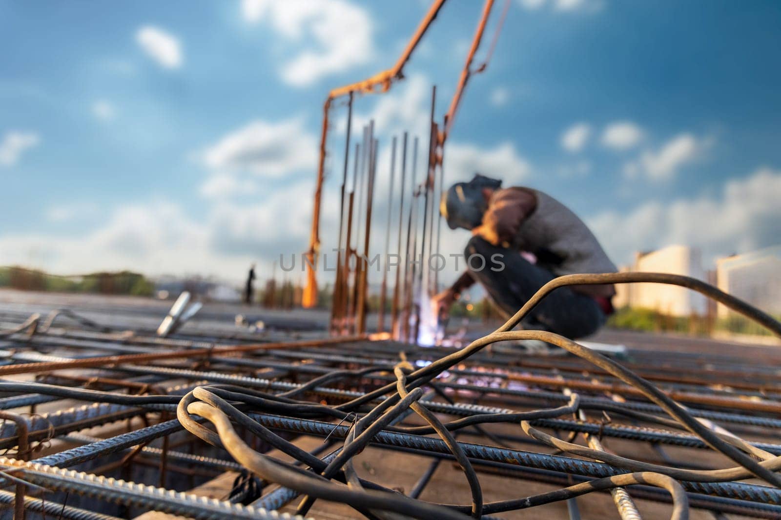 Welder electric welds a steel frame made of reinforcement for reinforced concrete structures at a construction site, selective soft focus.