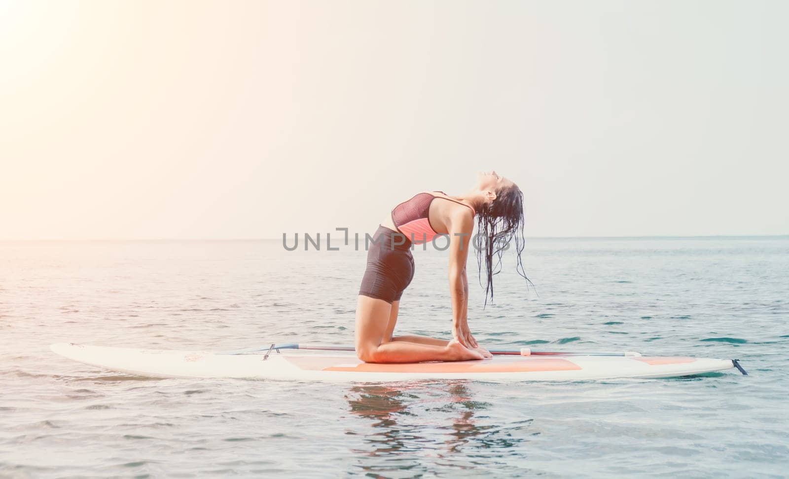 Woman sup yoga. Happy young sporty woman practising yoga pilates on paddle sup surfboard. Female stretching doing workout on sea water. Modern individual female outdoor summer sport activity