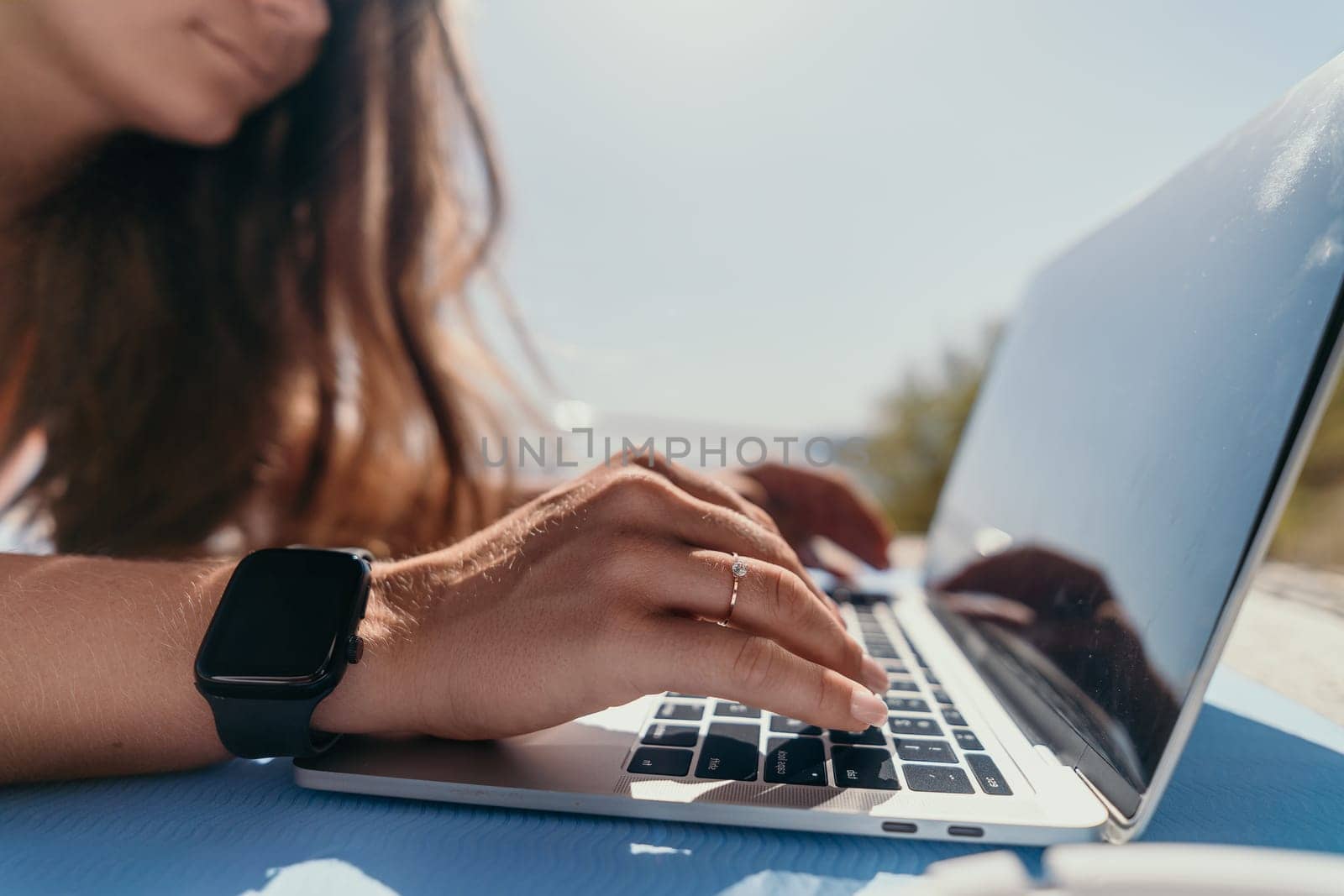 Digital nomad, Business woman working on laptop by the sea. Pretty lady typing on computer by the sea at sunset, makes a business transaction online from a distance. Freelance, remote work on vacation