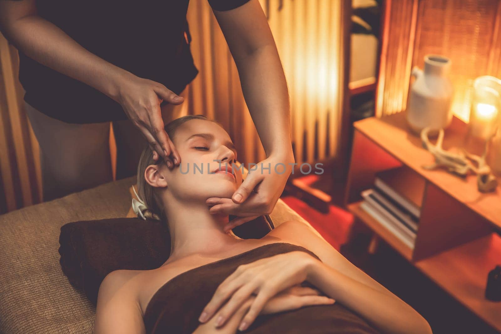 Caucasian woman enjoying relaxing anti-stress head massage and pampering facial beauty skin recreation leisure in warm candle lighting ambient salon spa in luxury resort or hotel. Quiescent