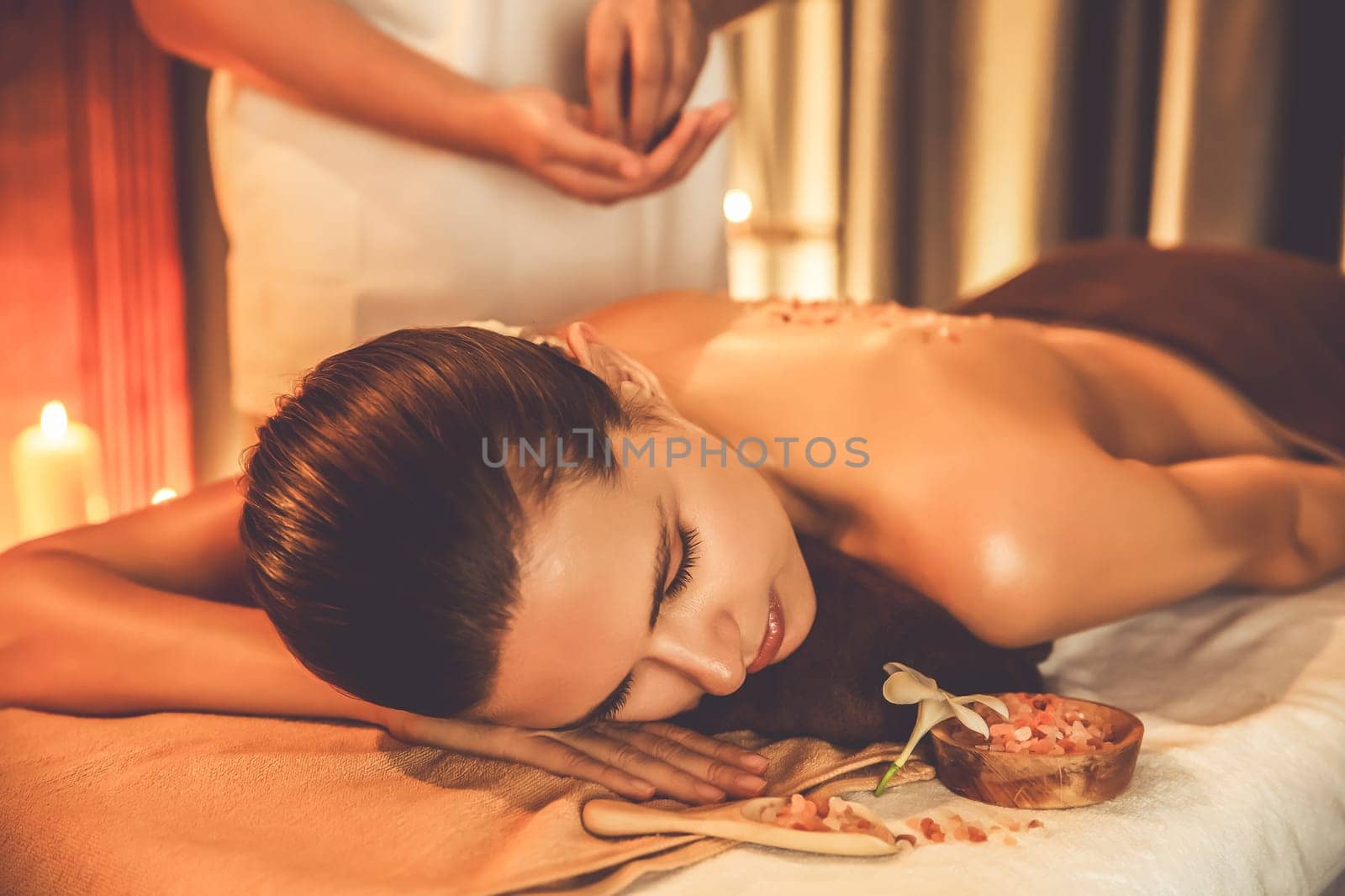 Woman customer having exfoliation treatment in luxury spa salon with warmth candle light ambient. Salt scrub beauty treatment in Health spa body scrub. Quiescent