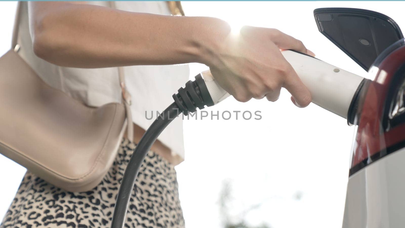 Sunlight backlit brighten young woman travel with EV electric car charging in green sustainable city outdoor garden in summer. Green urban sustainability lifestyle by electric vehicle innards