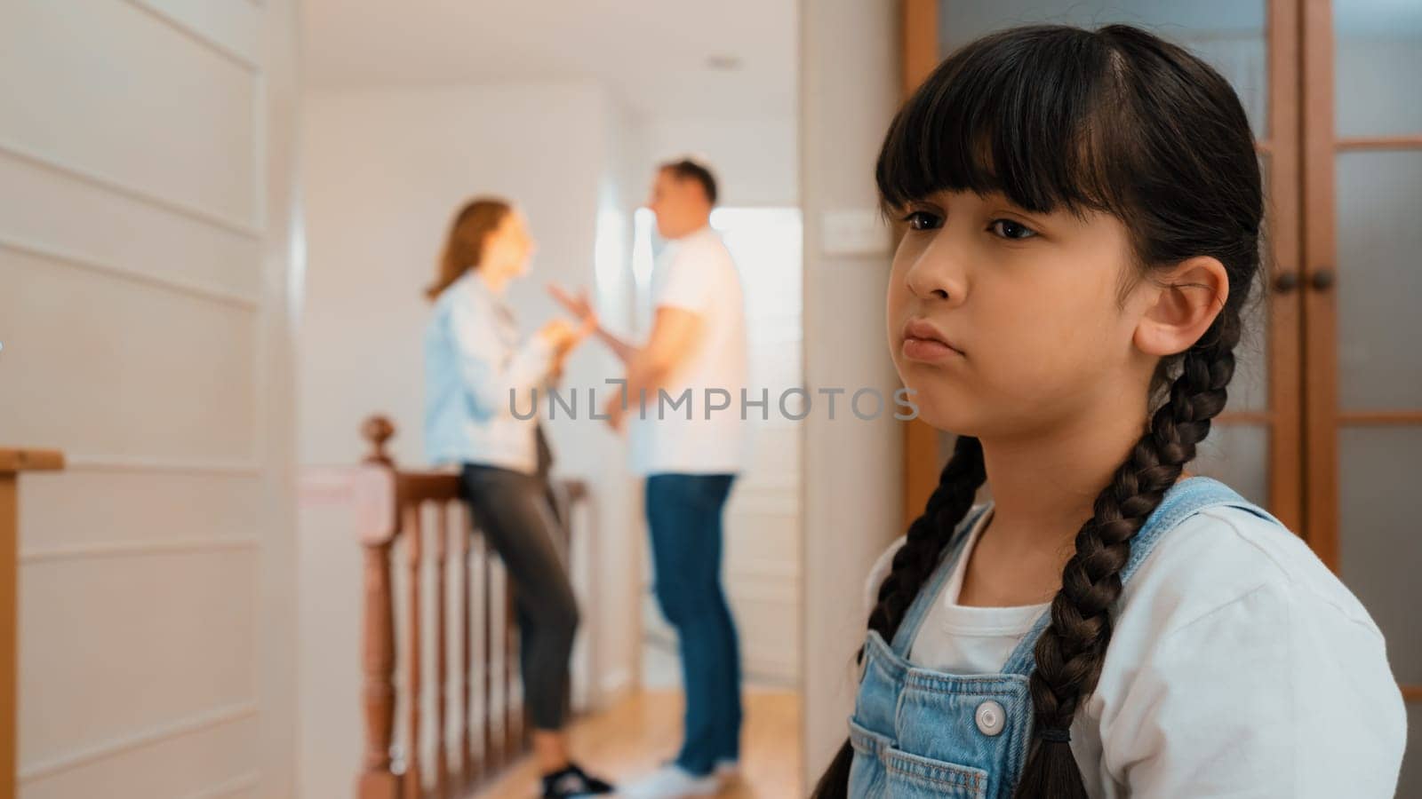 Stressed and unhappy young girl huddle in corner crying and sad while her parent arguing in background. Domestic violence at home and traumatic childhood develop to depression. Synchronos