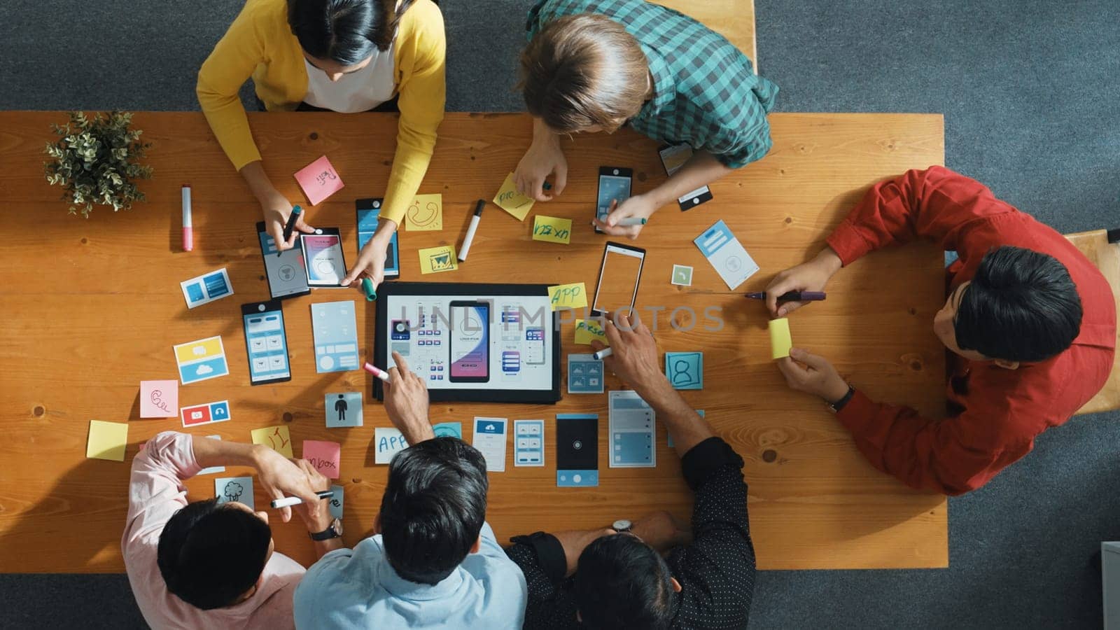 Top view of software developer team looking Ux Ui design for mobile phone interface from tablet while comparing and planning wireframe prototype designing together at creative workplace. Convocation.