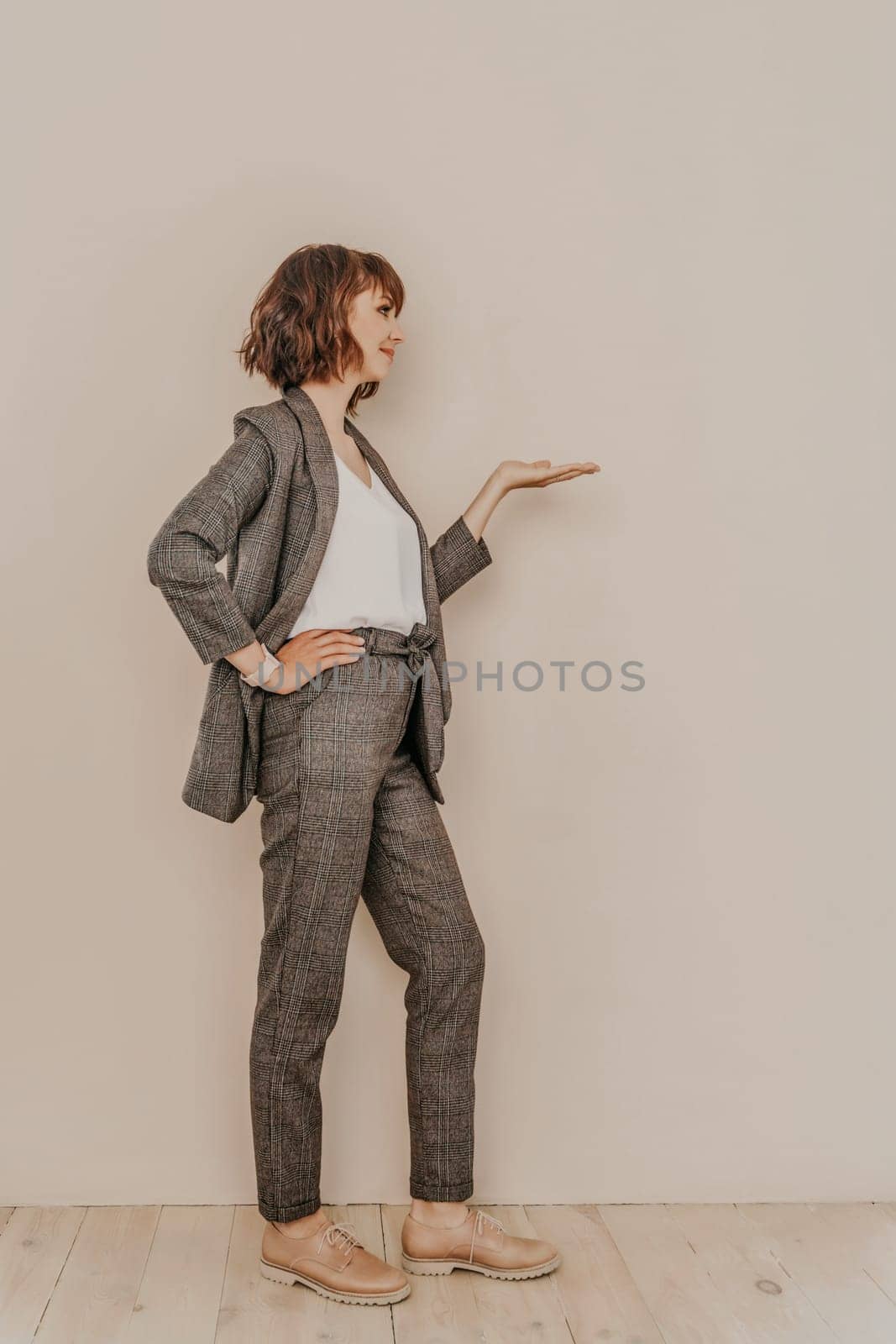 Brunette suit wall. Business woman in a beige suit posing on a beige background. Full length studio portrait