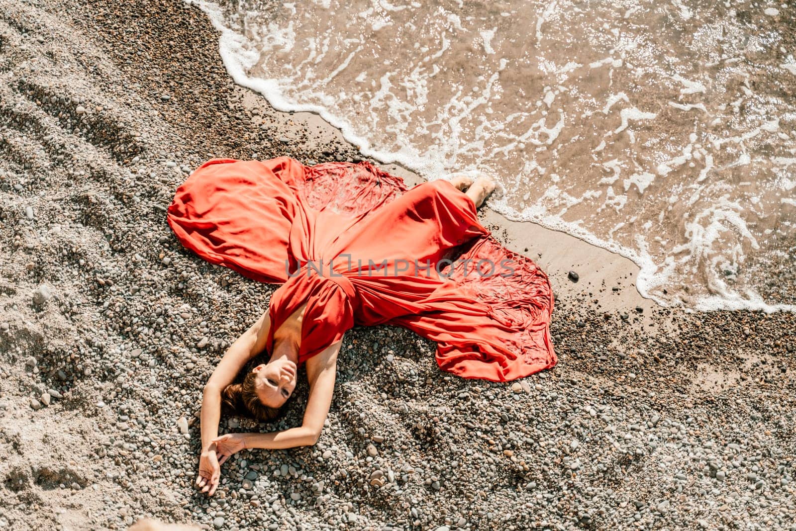 Woman red dress sea. Female dancer in a long red dress posing on a beach with rocks on sunny day.