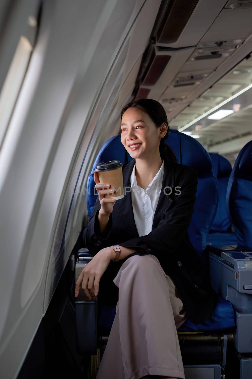 Young Asian woman sitting near the window on a business class airplane during a flight. Travel and business concept. by wichayada