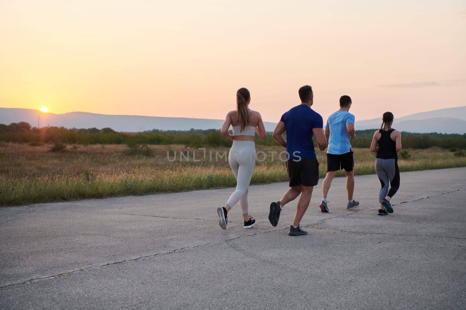 A diverse group of runners finds motivation and inspiration in each other as they train together for an upcoming competition, set against a breathtaking sunset backdrop.