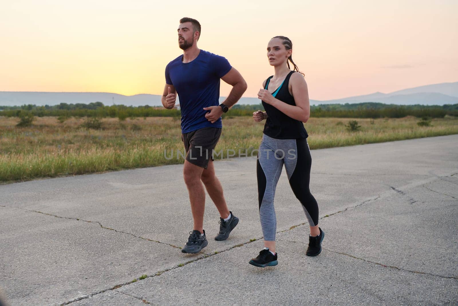 A vibrant couple dashes running the outdoors, embodying the essence of athleticism and romance, their confident strides reflecting a shared commitment to fitness and preparation for future marathon challenges.