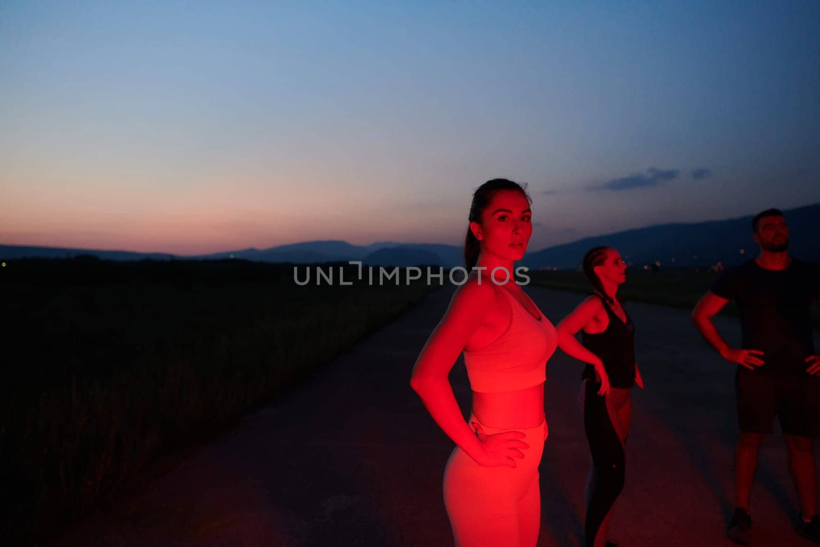 After a grueling nighttime run, an athlete strikes a confident pose, bathed in the red glow of the surroundings, showcasing both exhaustion and determination.