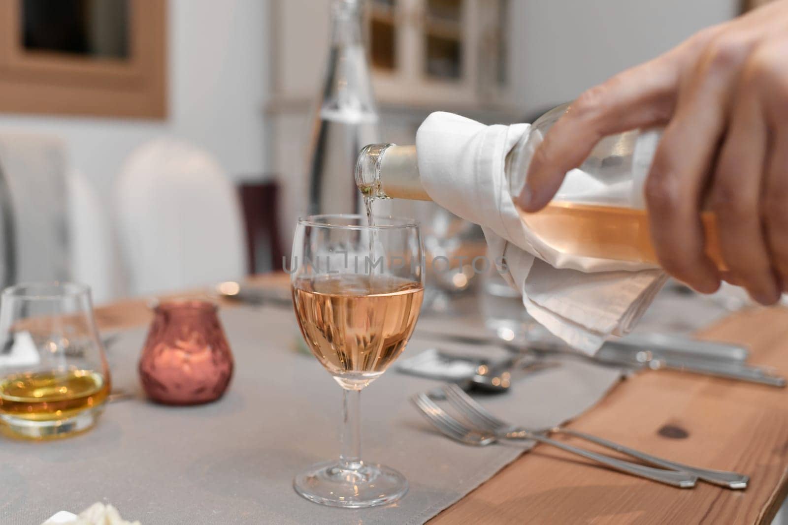 A waiter pours the pink french wine into the glass by Godi