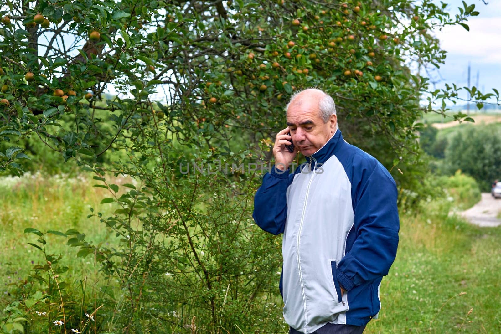 Elderly retired man walking talking on the phone in a august september garden by jovani68