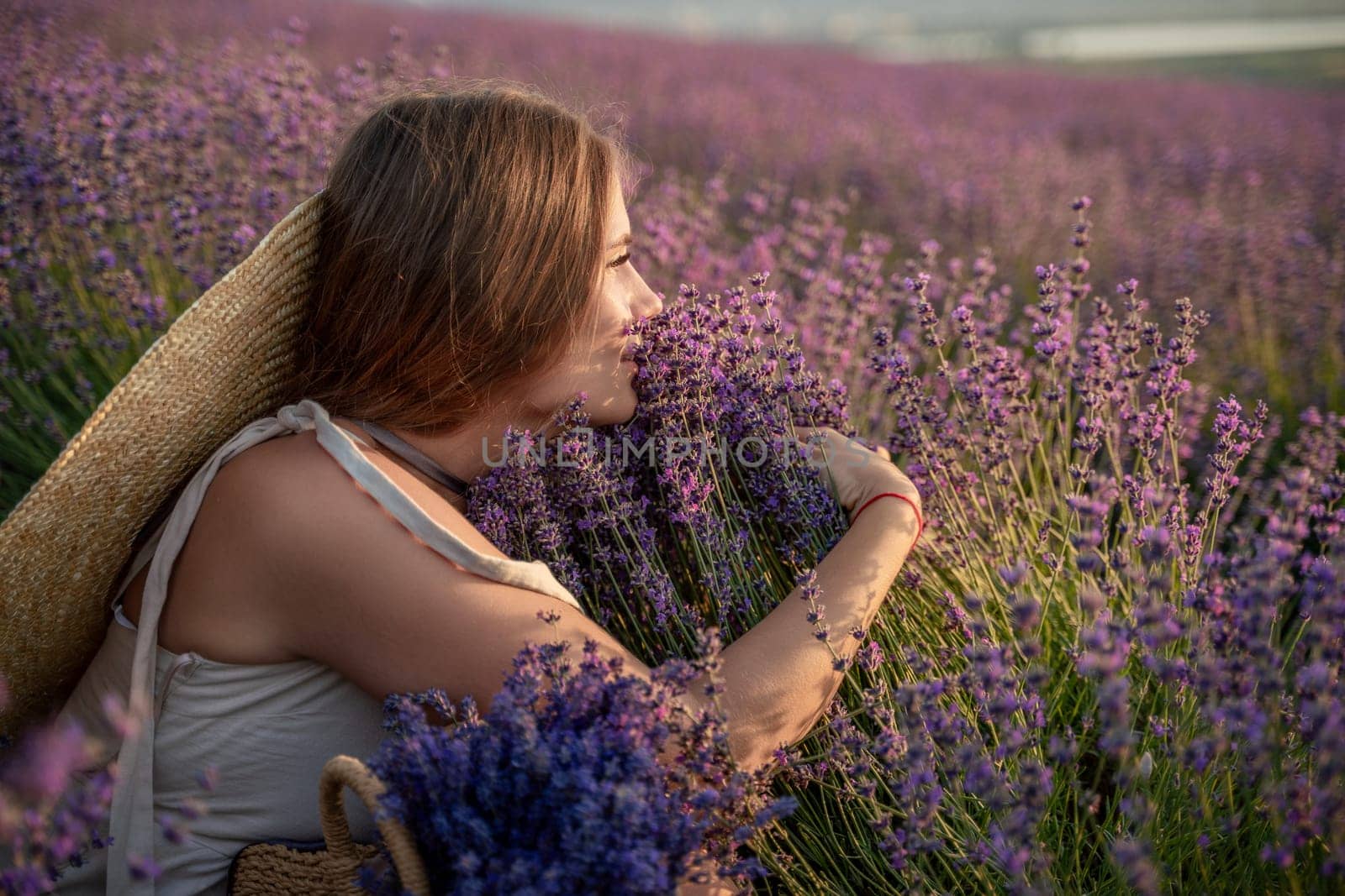 A woman is sitting in a field of lavender flowers. She is wearing a straw hat and holding a basket of flowers. The scene is peaceful and serene, with the woman enjoying the beauty of the flowers. by Matiunina