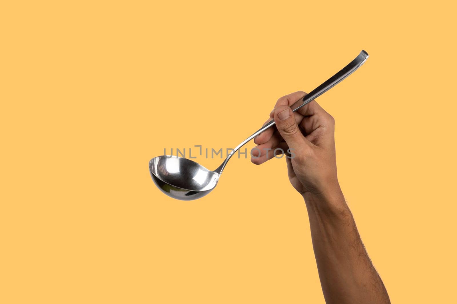 Black male hand holding a silver kitchen ladle isolated o yellow background by TropicalNinjaStudio