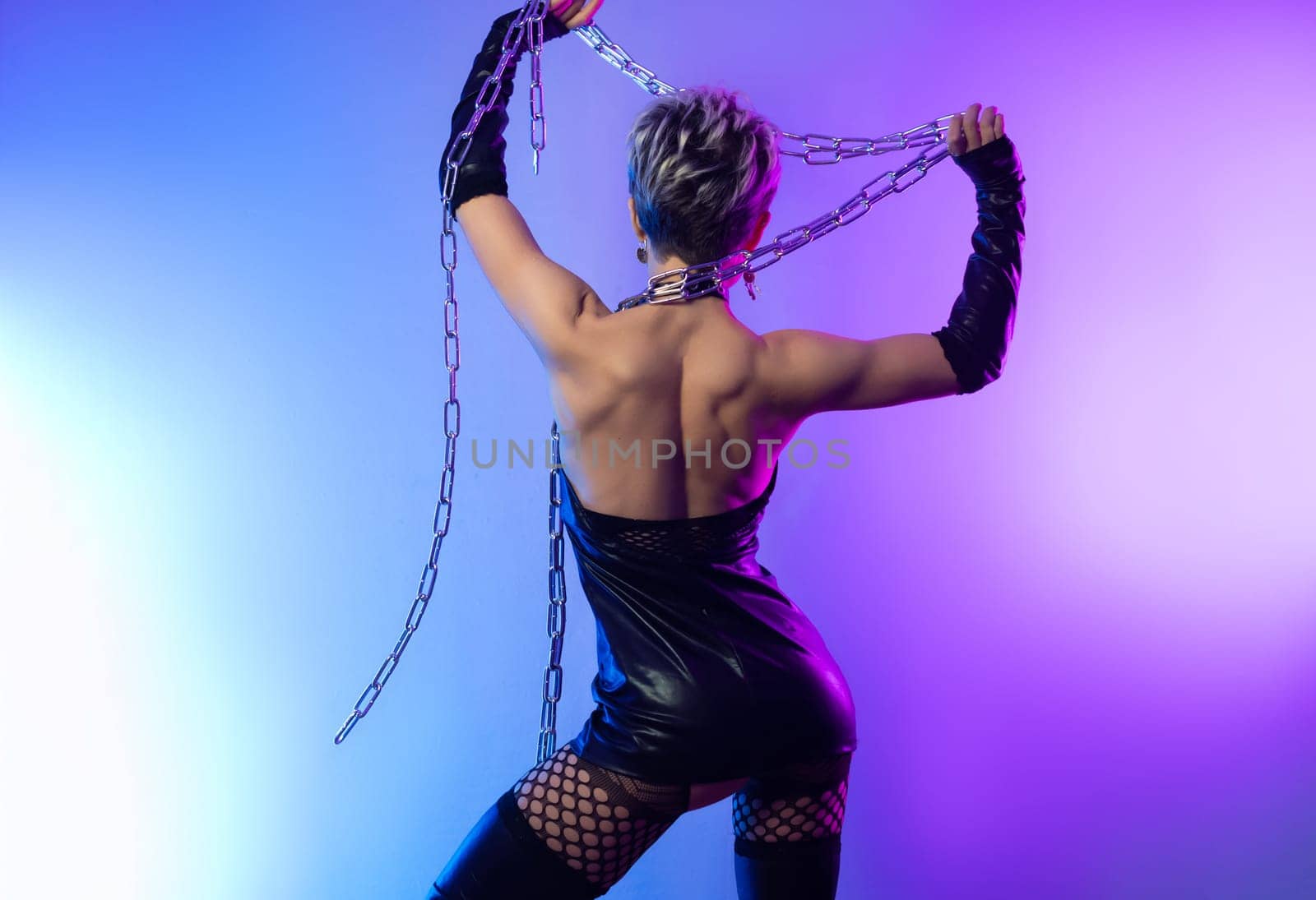 sexy girl in the erotic image of a bdsm mistress in leather belts with a metal chain shackles poses against a background of copy paste in a beautiful neon background of copy paste