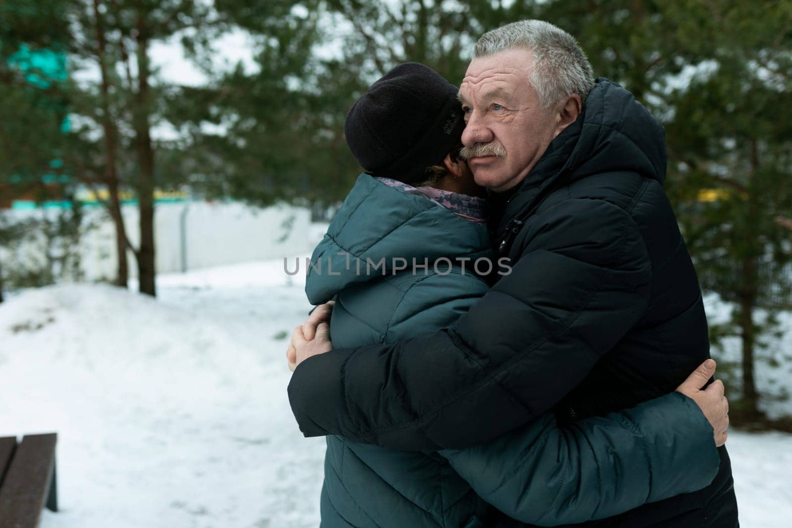 Cute retired couple walking in the park and hugging each other in winter park.