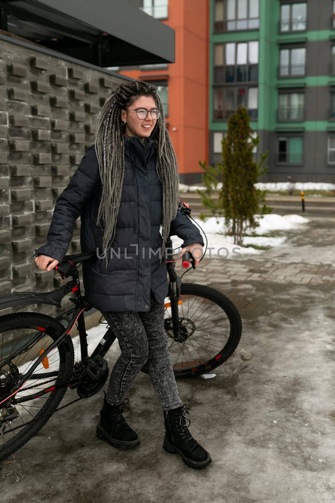 Lifestyle concept, a young pretty European woman with pigtails dressed in a warm winter jacket rides around the city on a bicycle.