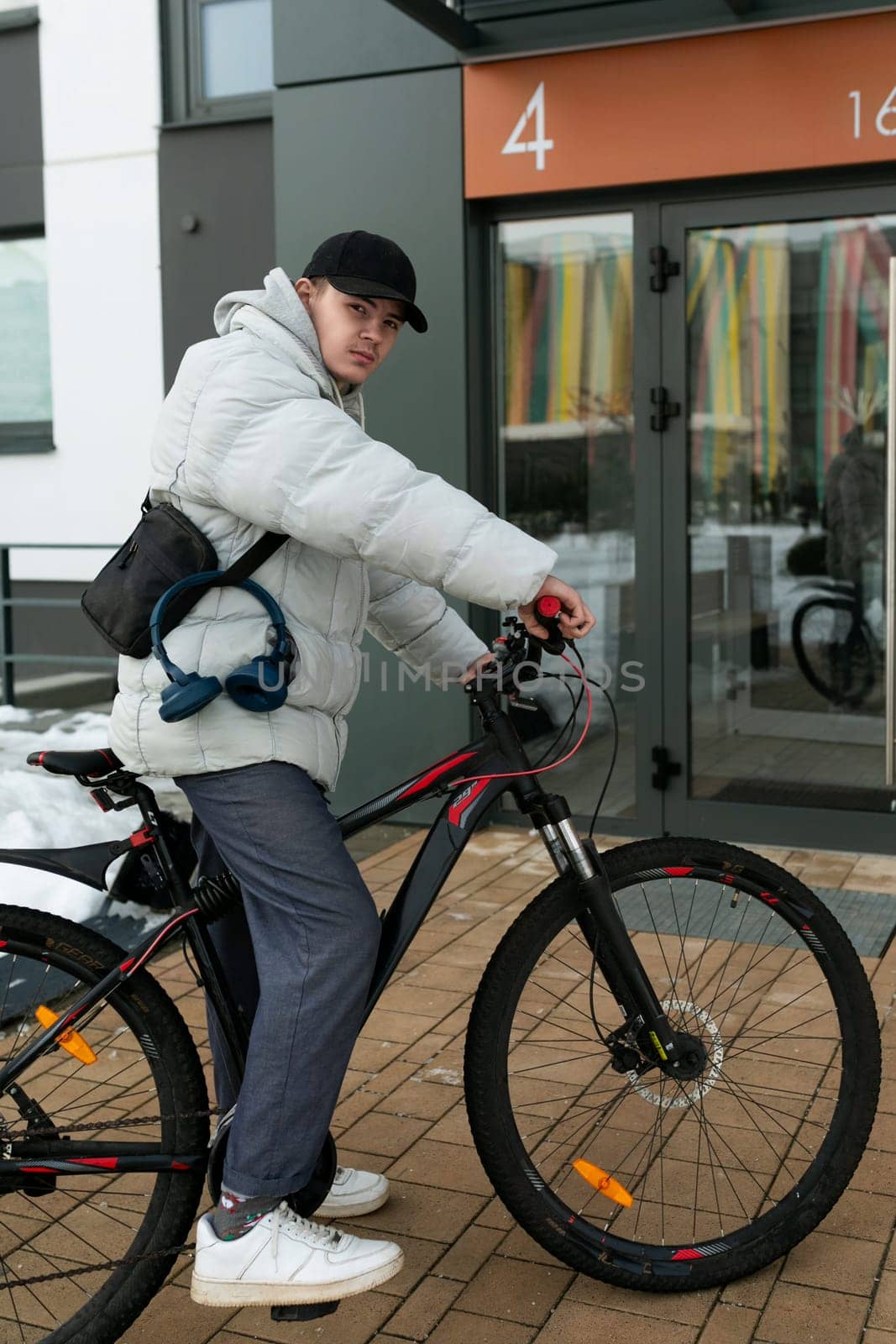 A young man in autumn clothes is waiting for a friend with a bicycle on the street by TRMK