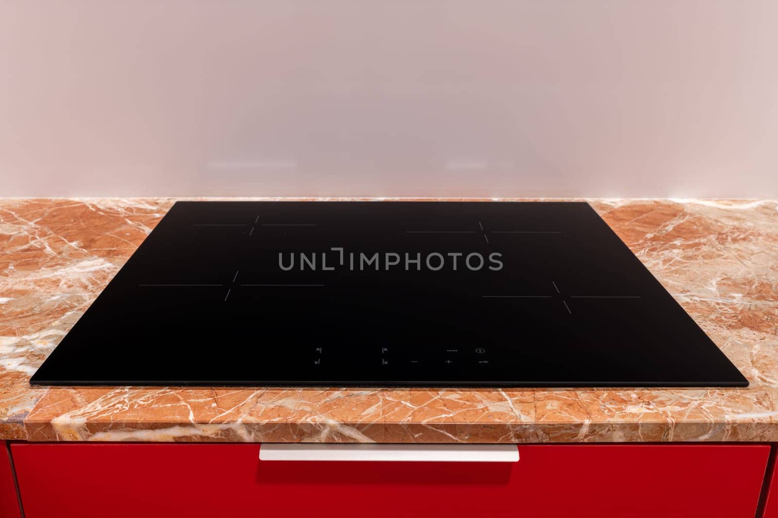 Sleek modern induction cooktop on a marble counter against a red backdrop by apavlin
