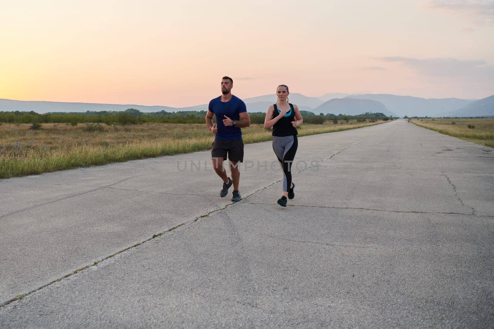 A vibrant couple dashes running the outdoors, embodying the essence of athleticism and romance, their confident strides reflecting a shared commitment to fitness and preparation for future marathon challenges.