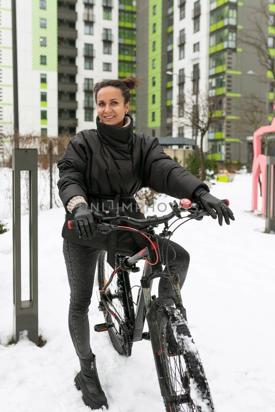 A young pretty woman in a winter jacket rented a bicycle and is riding it.