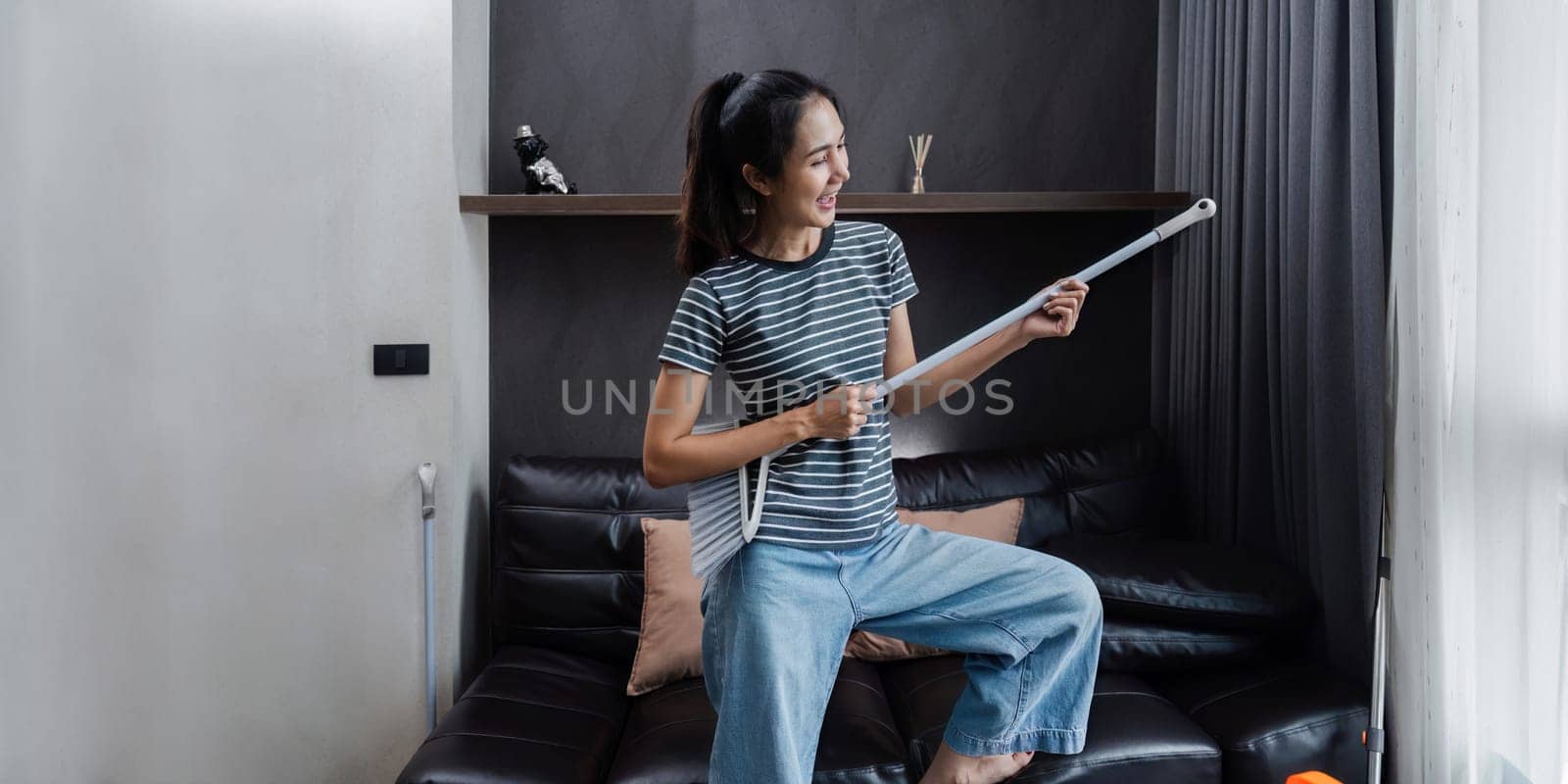 young asian woman having fun during cleaning, fooling with mop and broom.