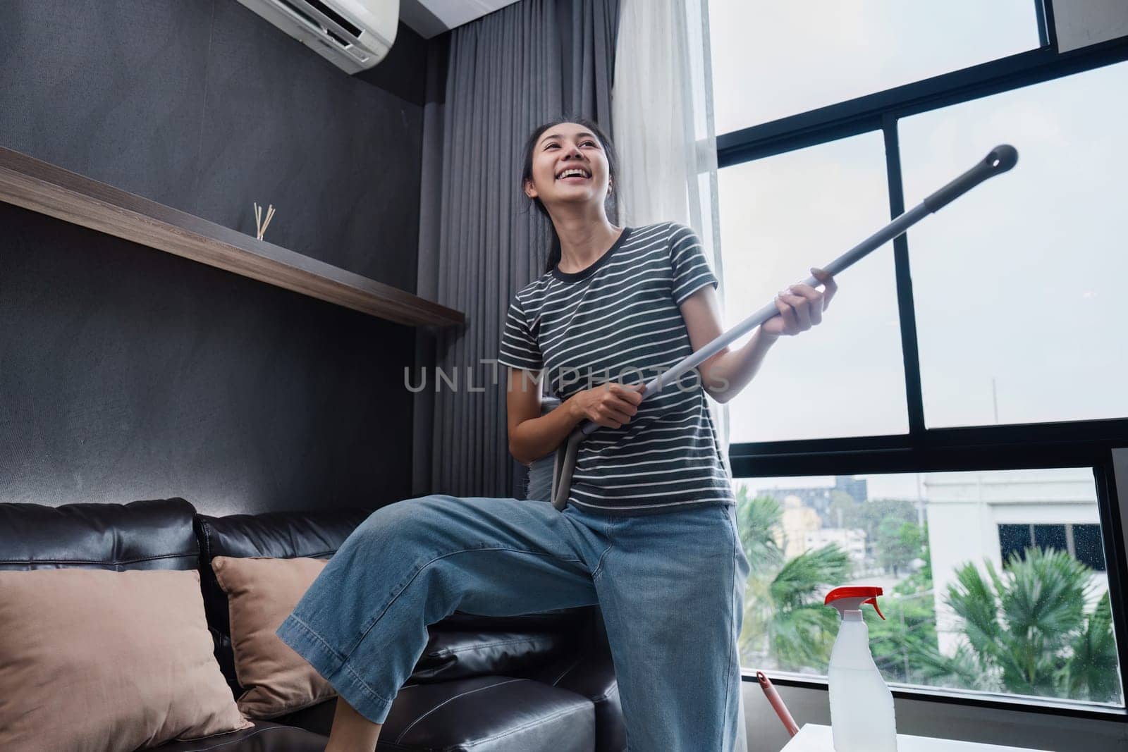 young asian woman having fun during cleaning, fooling with mop and broom.