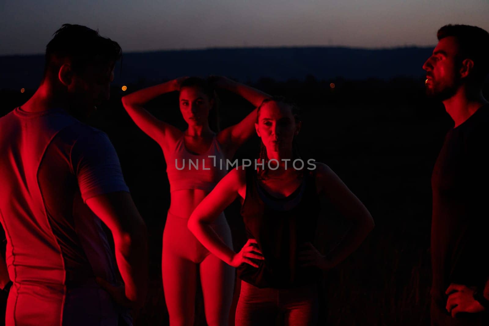 Diverse Athletes Unwind: Post-Marathon Rest Under Red Nighttime Glow. by dotshock