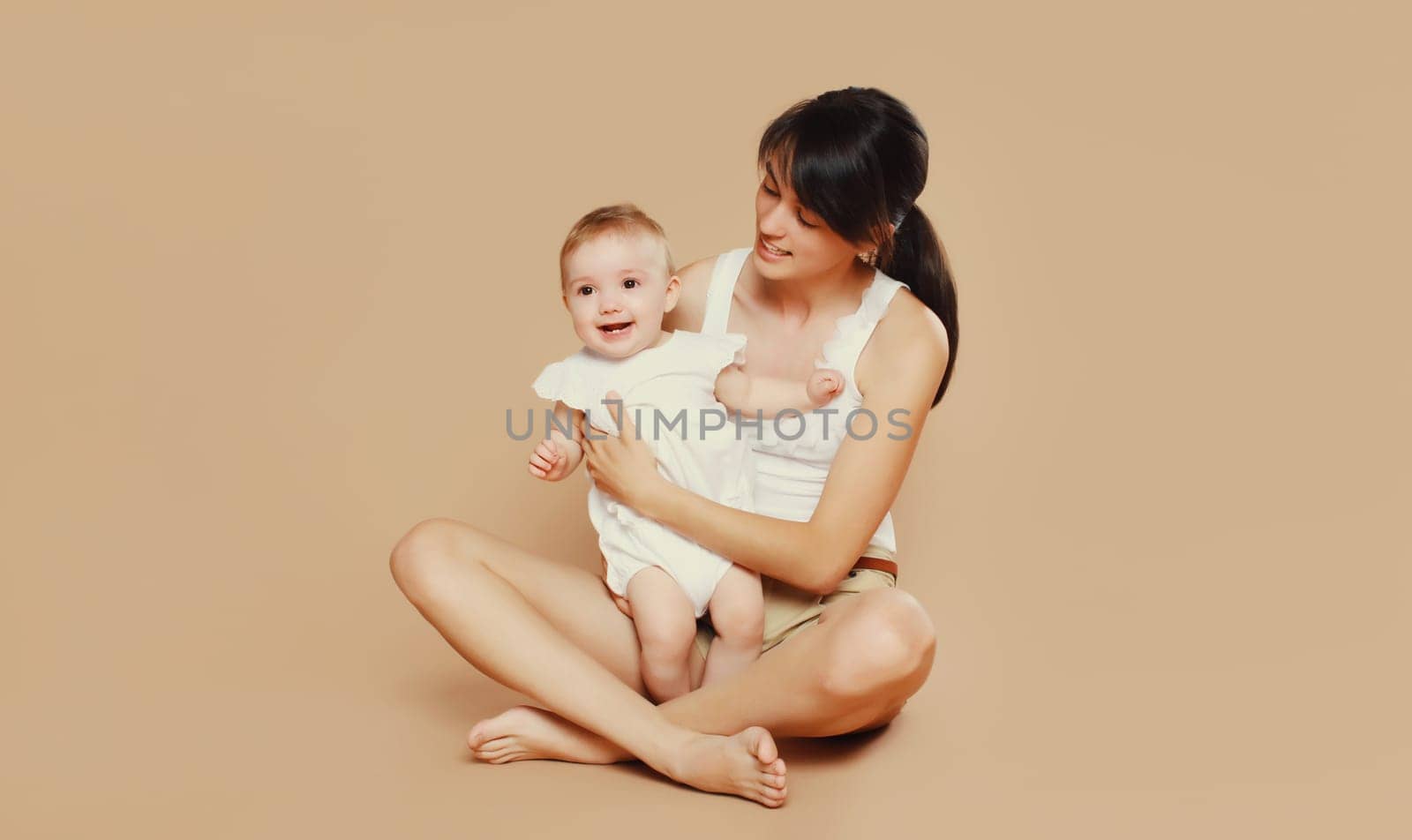 Happy cheerful young mother playing with cute baby on brown studio background by Rohappy