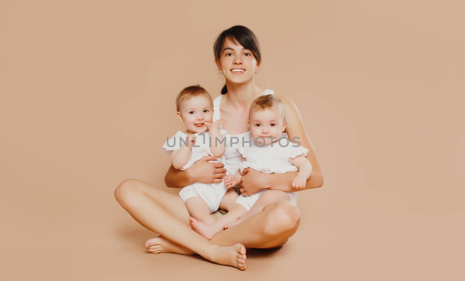Happy cheerful smiling young mother holding baby on brown studio background