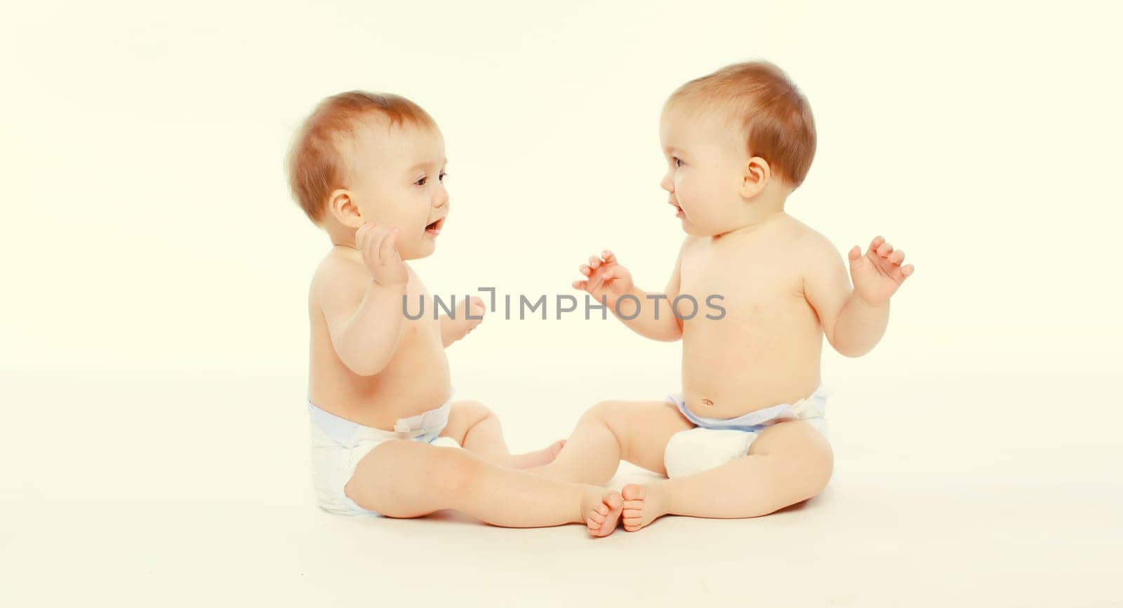Cute two twin babies in diapers sitting on the floor on white studio background