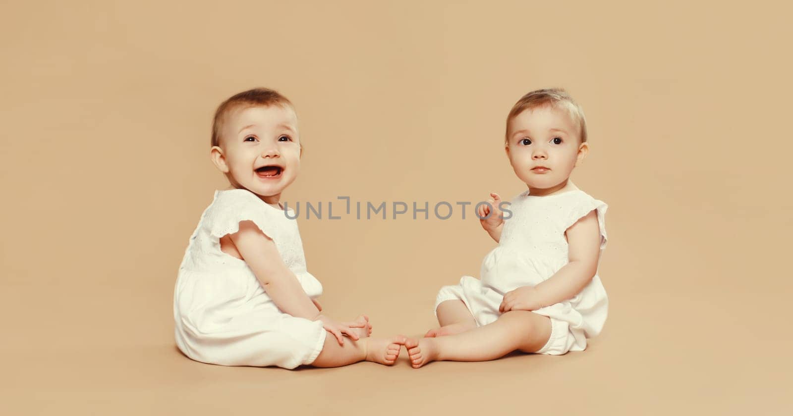 Happy cute two twin babies sitting on the floor on brown studio background by Rohappy