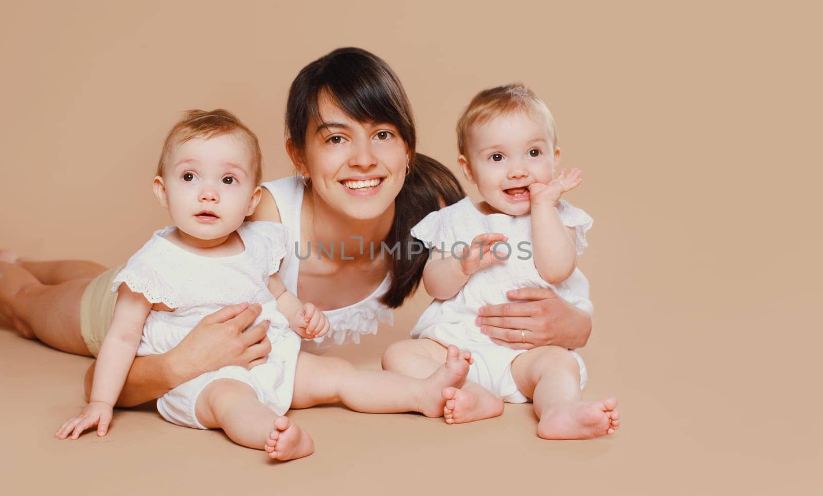 Happy cheerful smiling young mother holding baby on brown studio background