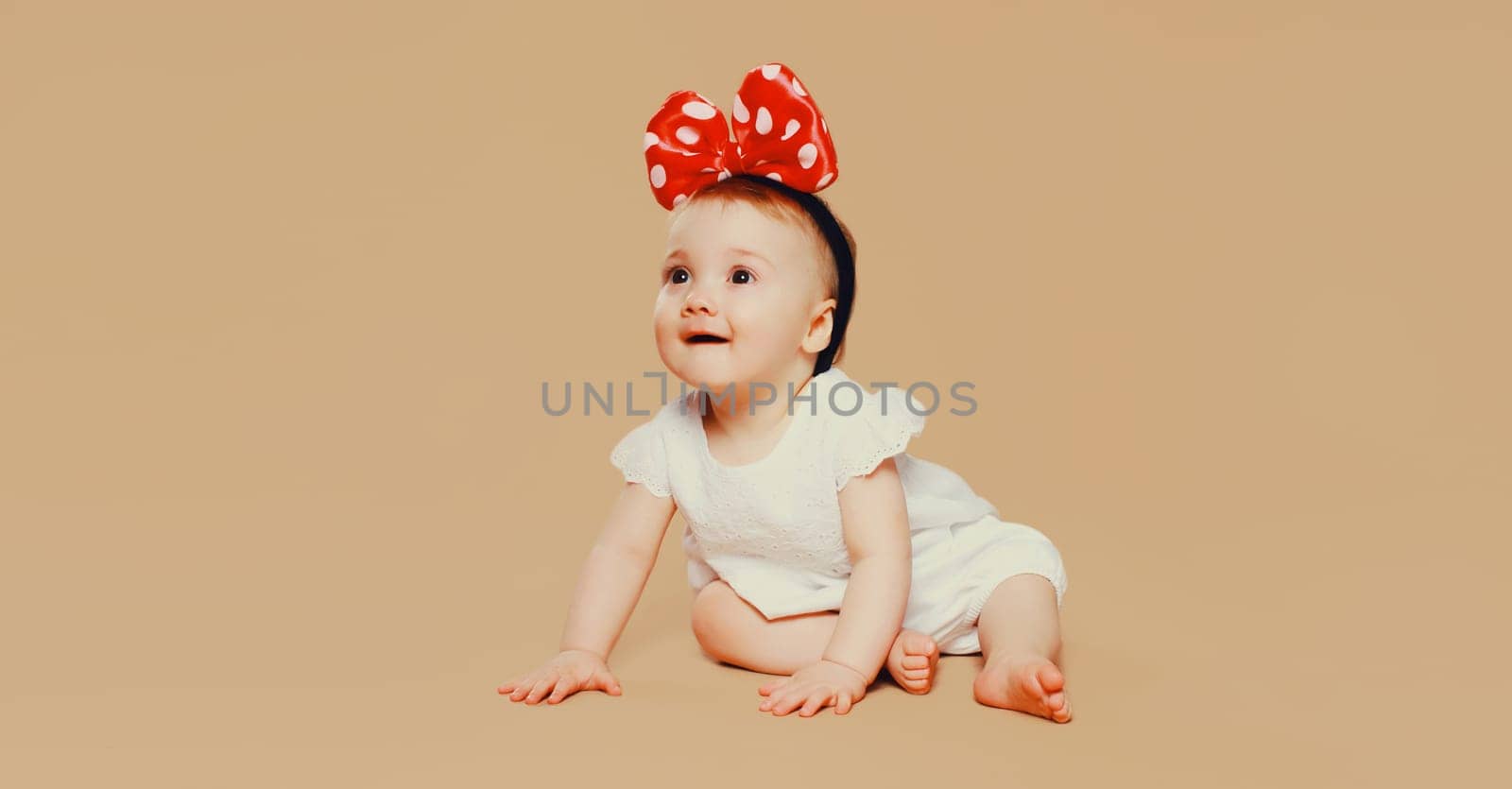 happy cute baby with bow on the head crawling on the floor on brown studio background