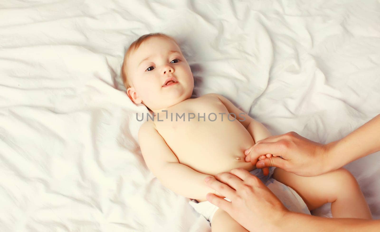 mother gives massage to baby lying on the bed at home, child and health concept