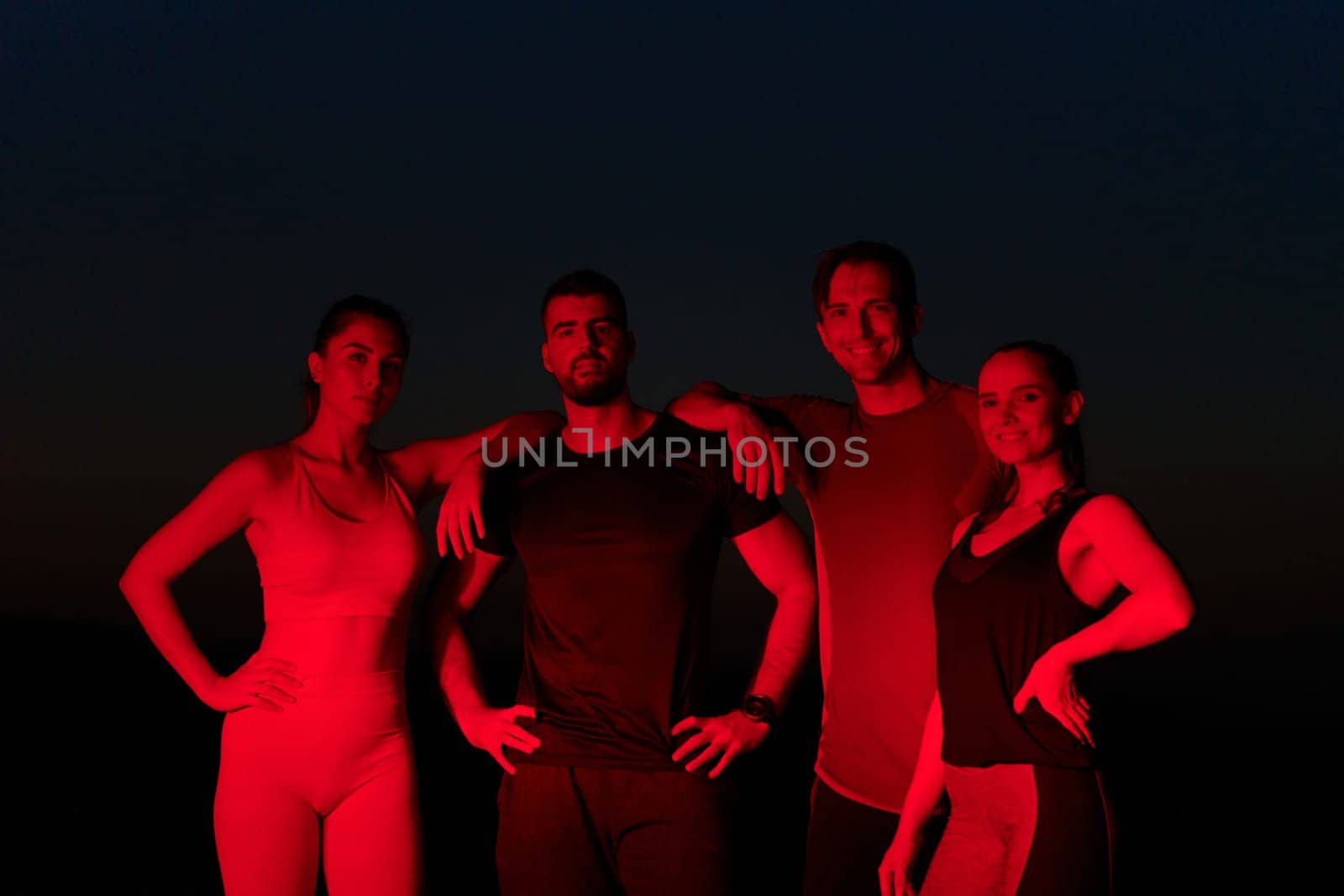 In the late-night hours, a diverse group of exhausted athletes find solace under a red glow, reflecting on their day-long marathon journey and celebrating camaraderie amidst fatigue.