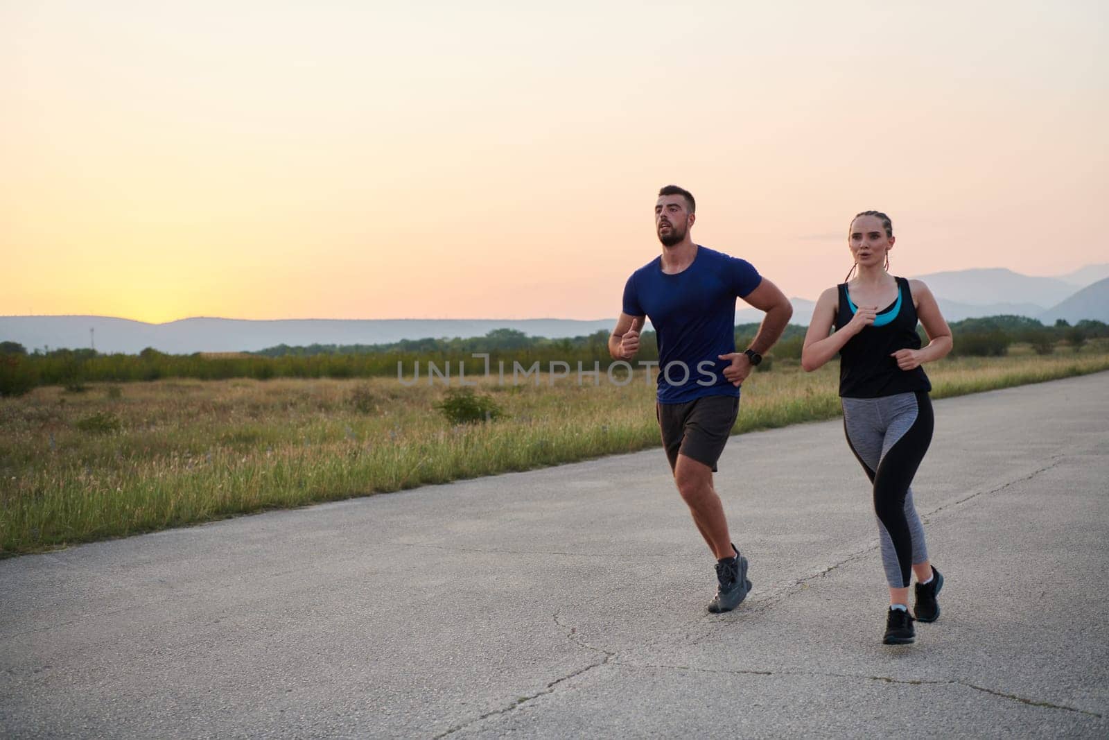 A vibrant couple dashes running the outdoors, embodying the essence of athleticism and romance, their confident strides reflecting a shared commitment to fitness and preparation for future marathon challenges.