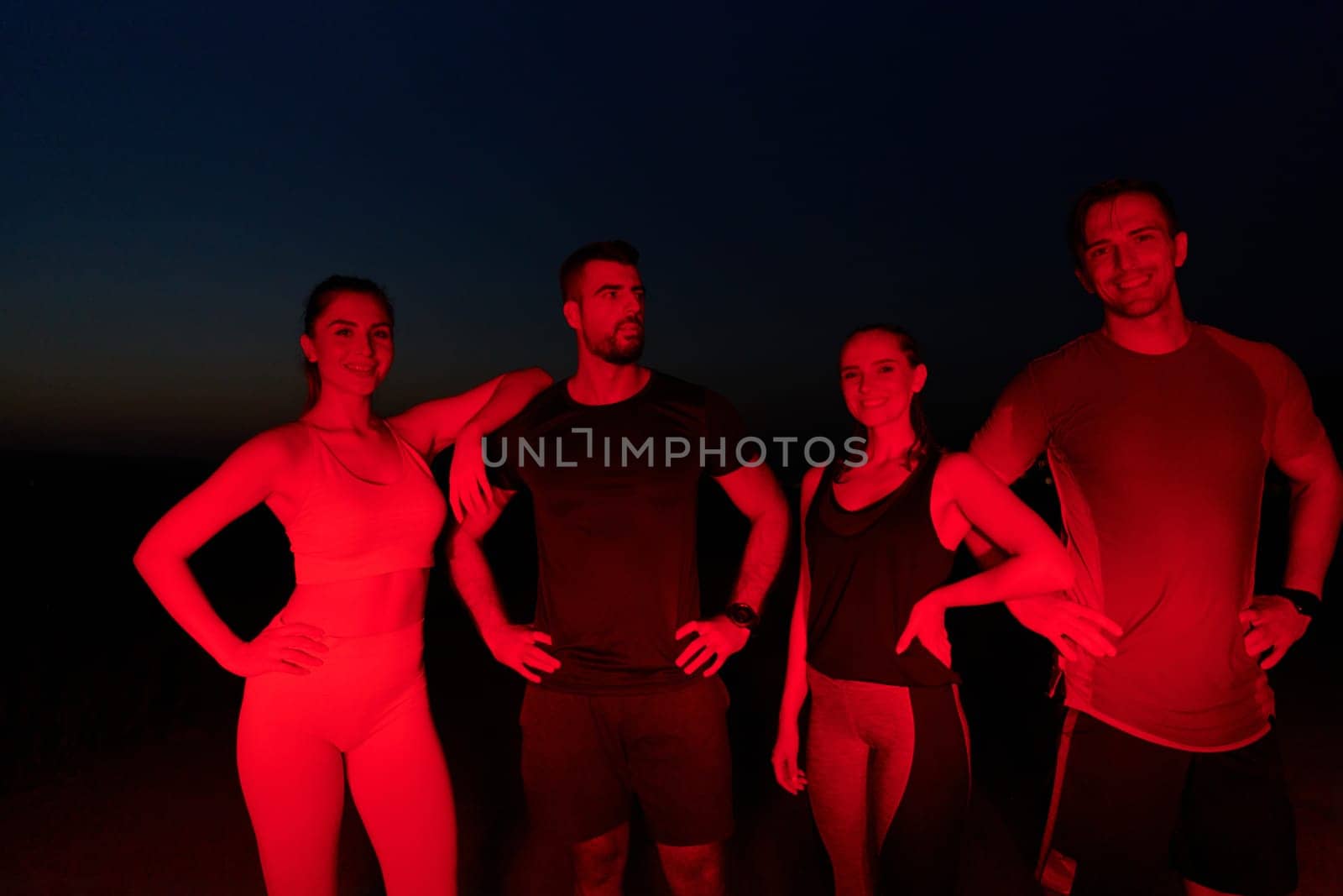 In the late-night hours, a diverse group of exhausted athletes find solace under a red glow, reflecting on their day-long marathon journey and celebrating camaraderie amidst fatigue.