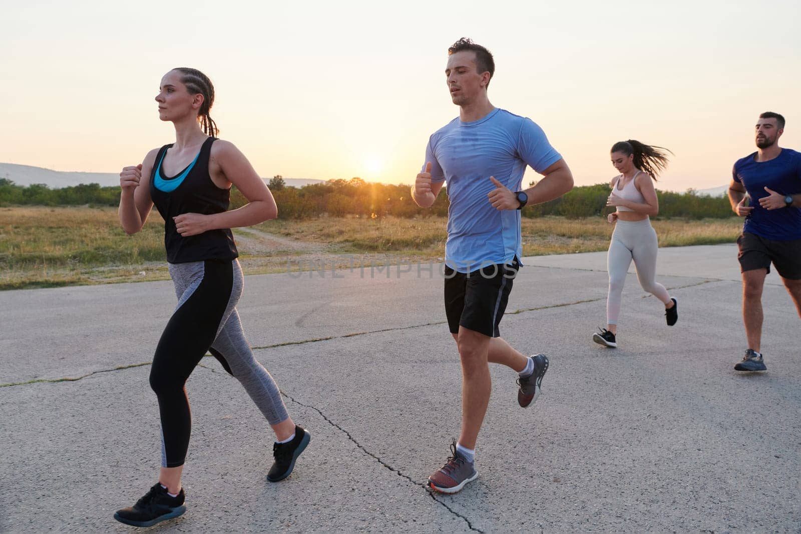 A diverse group of runners finds motivation and inspiration in each other as they train together for an upcoming competition, set against a breathtaking sunset backdrop.