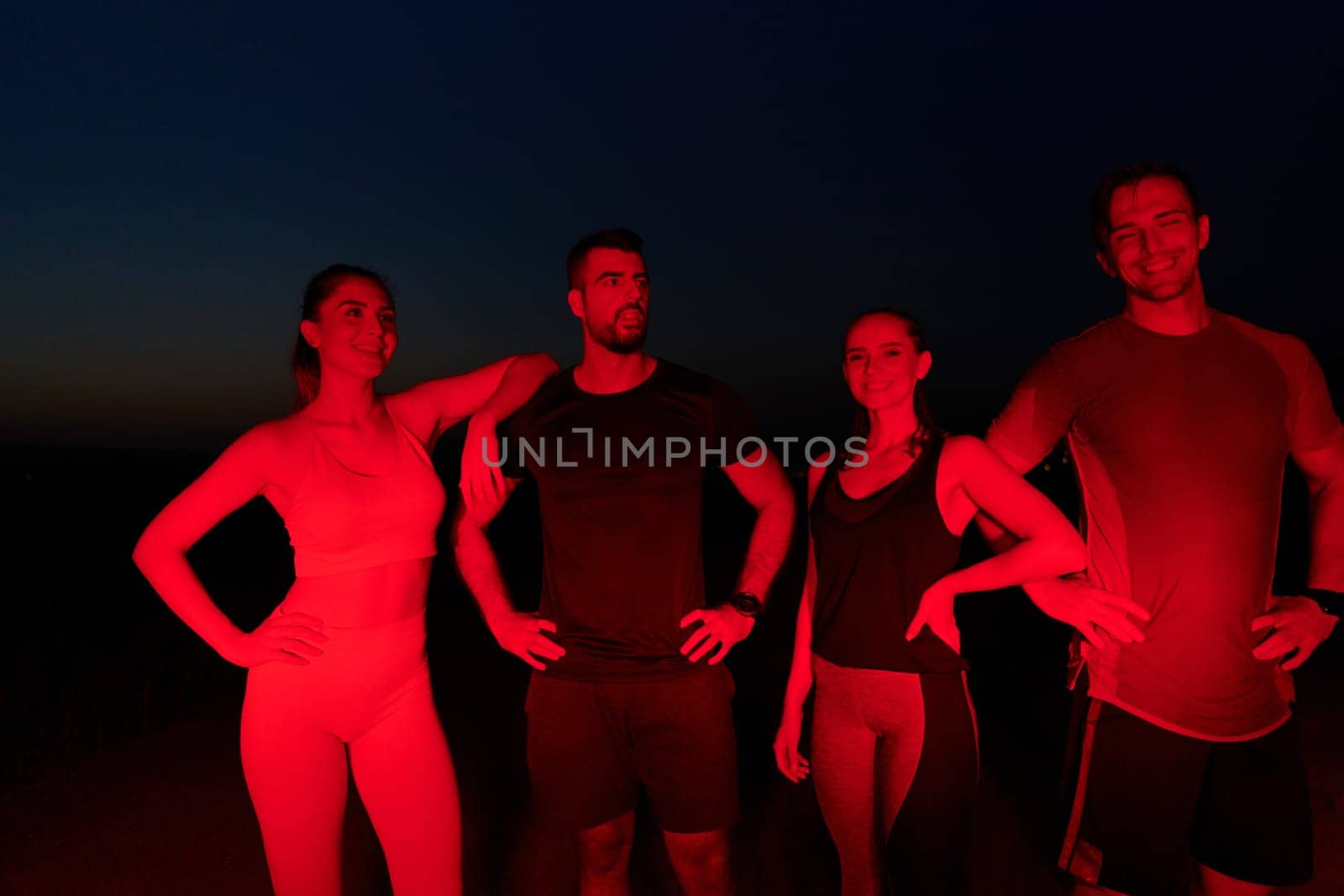 In the late-night hours, a diverse group of exhausted athletes find solace under a red glow, reflecting on their day-long marathon journey and celebrating camaraderie amidst fatigue.