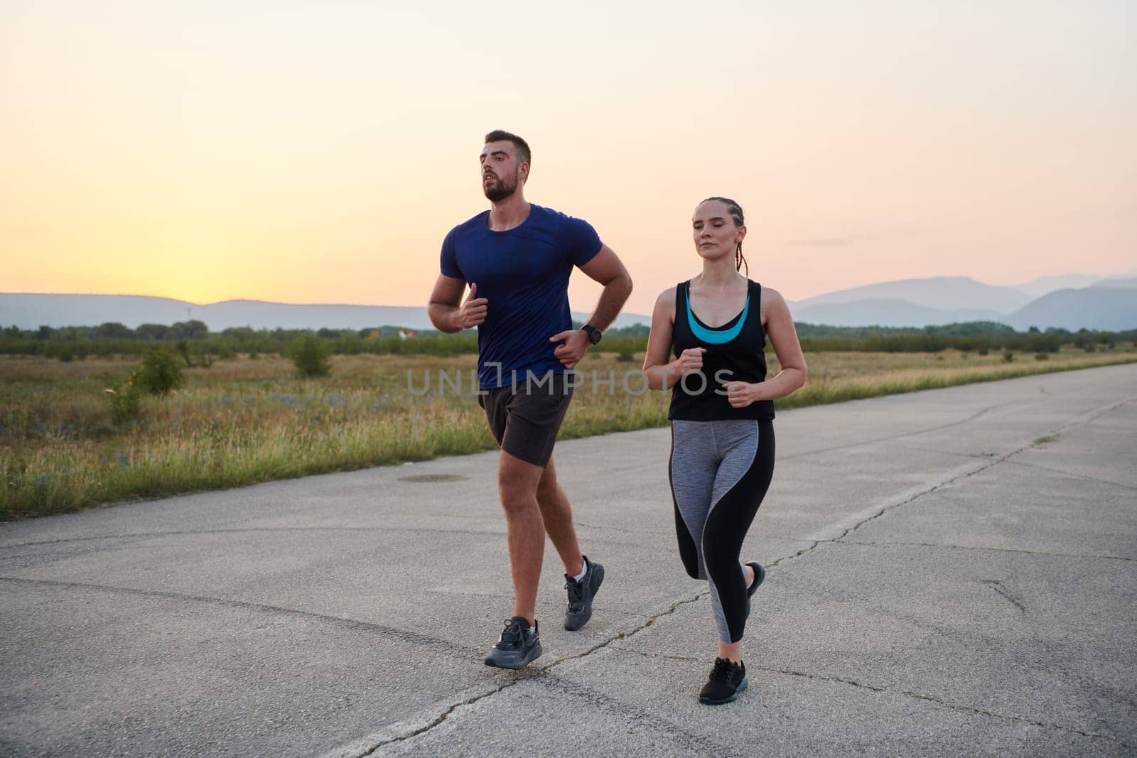 A vibrant couple dashes running the outdoors, embodying the essence of athleticism and romance, their confident strides reflecting a shared commitment to fitness and preparation for future marathon challenges.